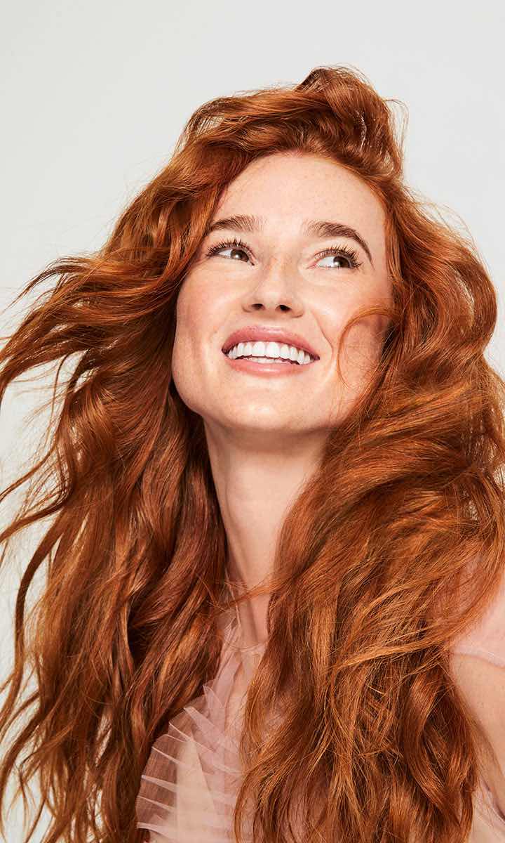 Woman with wavy red hair smiles with Cutting Crew Hair Salon's services.